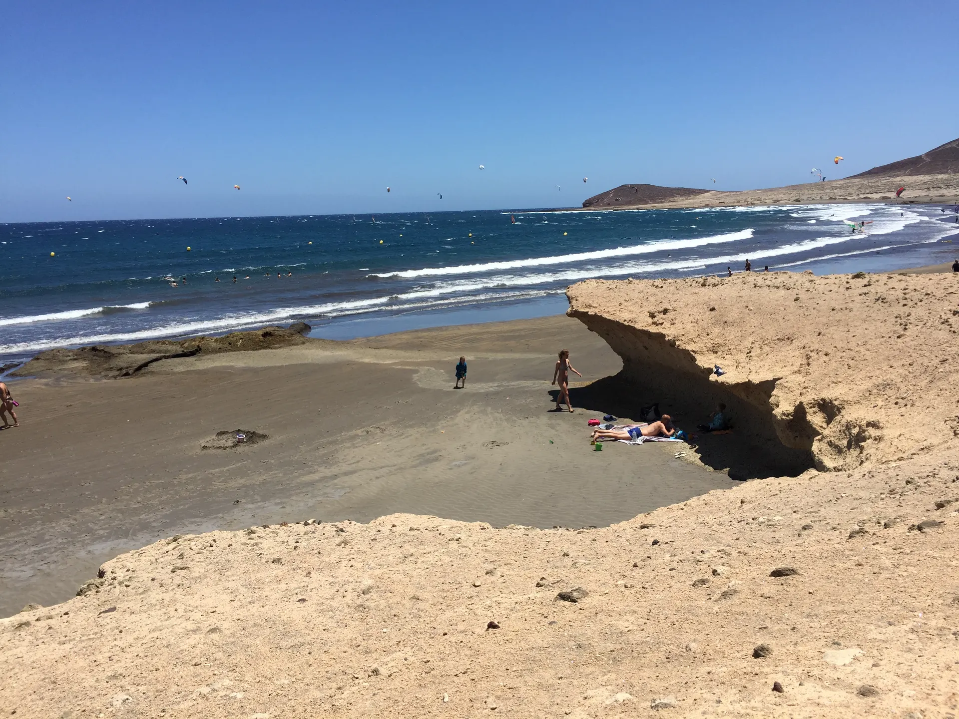Playa de El Médano con bañistas, kitesurfistas y Montaña Roja al fondo.